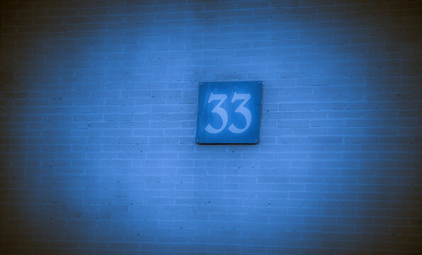 Number 33 sign fixed on a textured brick wall with a cool blue hue