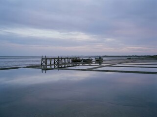 Fototapeta premium A serene coastal scene unfolds beneath a pastel sky, where wooden structure and boats find harmony with reflecting water.