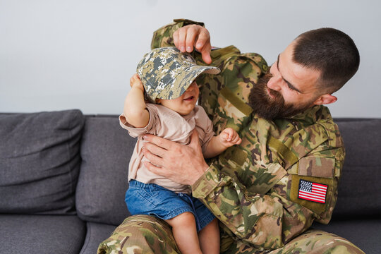American male soldier in military uniform returning home to family - Father having playful time with baby son - Homecoming, happiness and lifestyle concept