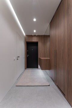 Contemporary entryway design featuring wood cabinetry, hidden storage, black front door and recessed lighting, minimalist corridor interior with elegant materials