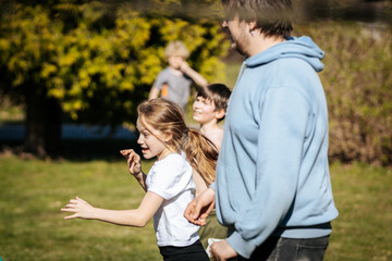 Fototapeta premium Group of children and adult running together in a park on a sunny day, with green grass and trees in the background creating a lively outdoor scene