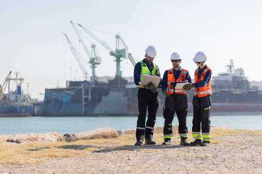 Workers discuss plans at a port with a cargo ship in the background