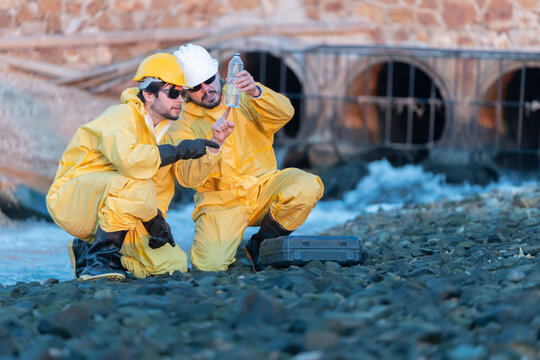 Workers collect water samples at a industrial site near a river during late afternoon