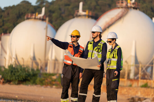 Petroleum engineers having a discussion near oil storage tanks
