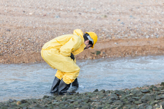 Workers in yellow suits and hard hats kneel by a river to collect water samples for testing at industrial site