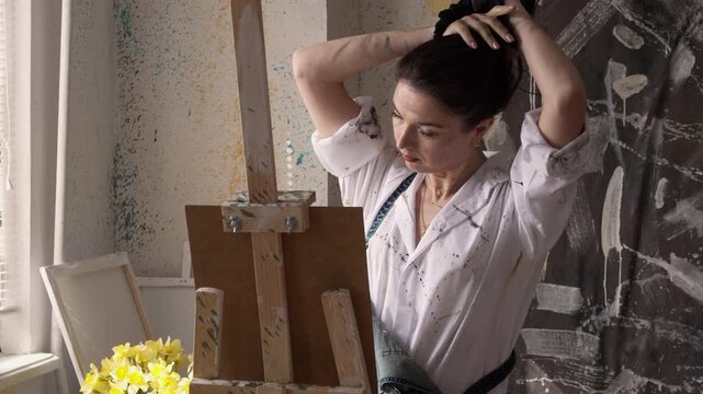 Woman artist tying her long hair in a ponytail before starting to paint a masterpiece in studio