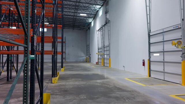 Empty Warehouse Interior with Tall Orange and Blue Shelving Racks, and closed loading dock doors