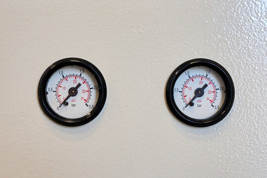 Two round pressure gauges mounted on a white wall. Industrial monitoring sensors showing bar and psi measurements for technical control systems.