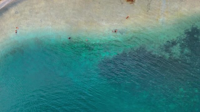 Swimmers in shallow turquoise water in Panama. Top-down drone view of swimmers in clear shallow water with sandy bottom, reef patches, and ripples.