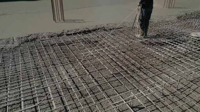 Construction worker using a poker vibrator to consolidate freshly poured wet concrete over a steel rebar mesh, ensuring a solid and compact foundation for a new building during its initial phase
