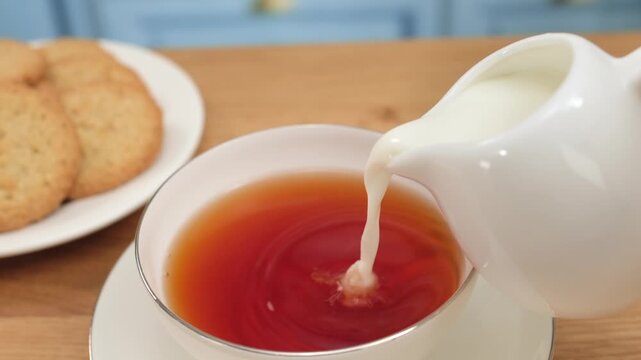 Cream pouring into hot tea creating soft swirl in white cup, copy space