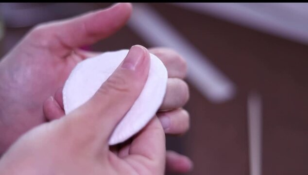 Close-up of hands cleaning fingernails with cotton pad, removing nail polish, static shot.
