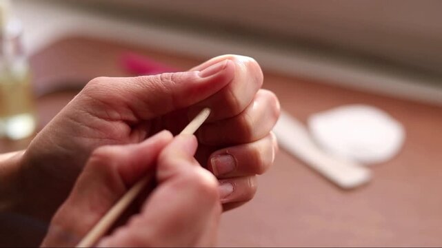 Close-up of female hands pushing cuticles with a wooden stick during self-manicure indoors, static