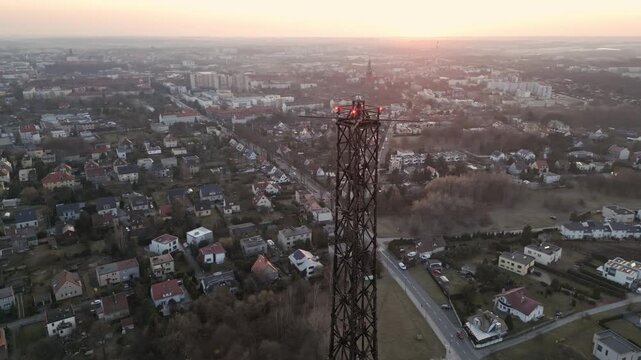 Aerial orbital drone flight circling the top of the Gliwice Radio Tower during sunset. The tallest wooden structure in the world with a city panorama in the background. Golden hour light.