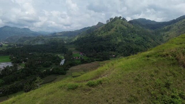 tunning aerial drone view of a sharp mountain ridge covered in lush green grass and pine trees under an overcast sky. Layers of forested hills and valleys extend into the misty distance, revealing th