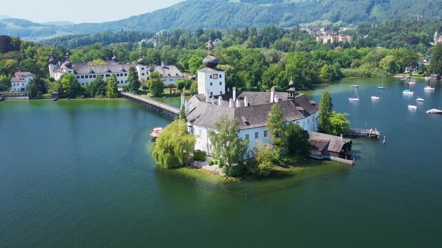 Aerial of beautiful white castle Ort Seeschloss in the Lake Traunsee, at Gmunden town. Serene lake, vibrant boats, and picturesque buildings along the shoreline. Austria tourism and scenic places