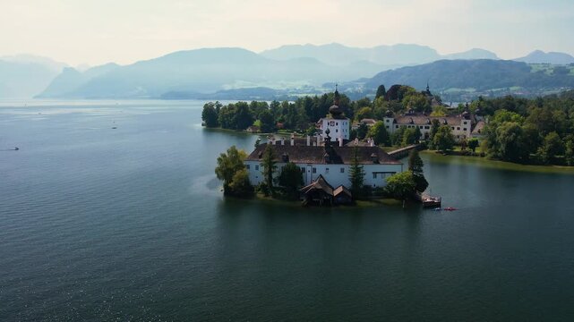 Aerial of beautiful white castle Ort Seeschloss in the Lake Traunsee, at Gmunden town. Serene lake, vibrant boats, and picturesque buildings along the shoreline. Austria tourism and scenic places