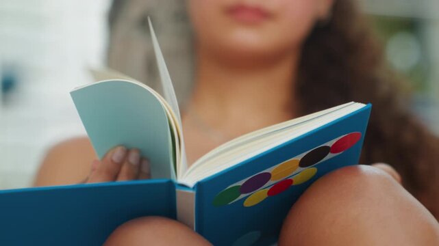 Young woman reading blue notebook on knees outdoors, closeup of hands turning pages, afternoon sun, resort palms, candid lifestyle shot showing rings and manicure, scenes suggest student, writer