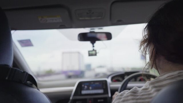 A woman driver navigates through highway traffic during her daily commute, viewed from the back seat of the car with a dashcam recording the journey ahead.