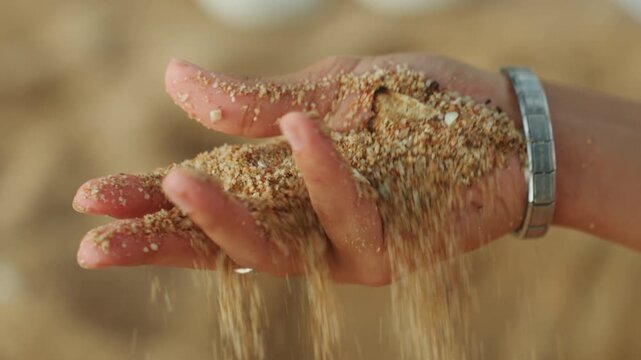 Open palm overflowing with coarse beach sand, silver bracelet accent, grains pouring and settling, warm sunlight and soft shadows, intimate closeup evoking memory and passing time, tactile detail