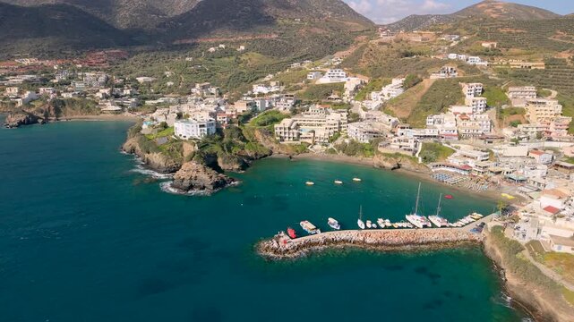 Aerial view of Bali village with white houses on hills and scenic harbor with boats. Panning shot to rugged rocky coastline and high mountains of Crete, Greece. Mediterranean landscape drone, 4k.