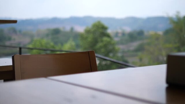 Cinematic blurred background of a serene mountain landscape from an outdoor cafe balcony, empty wooden table in foreground with copy space