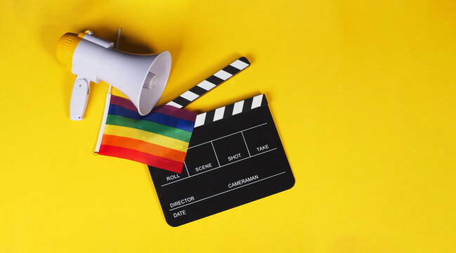 Clapper board and rainbow pride flag and megaphone on yellow background.