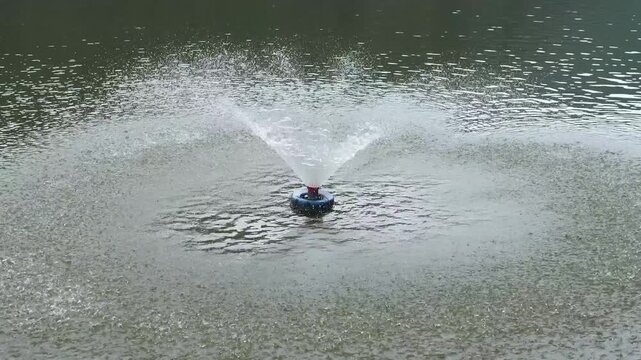 Cinematic shot of a floating water fountain aerator splashing and spraying water in a pond, surface aeration system for water quality and environmental management