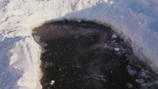 A hard chunk of compacted snow falls onto a dark frozen ice surface, slightly breaks apart on impact, and slides forward across the ice in a winter outdoor scene. High quality 4k footage