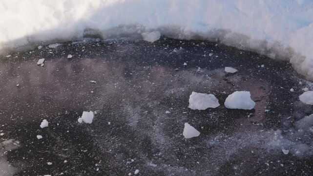 Several hard snow fragments rest on a dark icy surface after sliding across frozen ground, with small white pieces contrasting against the rough winter ice texture. High quality 4k footage