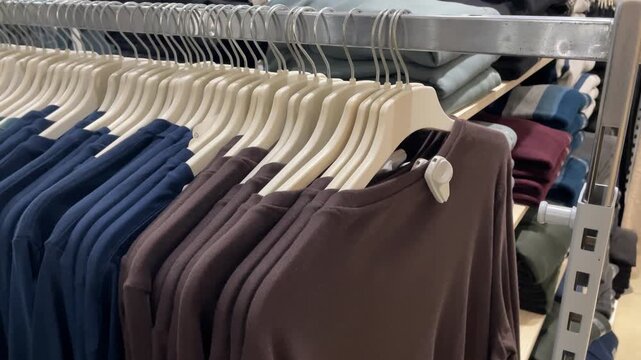 Clothing rack with various shirts organized by color in retail store setting emphasizing fashion