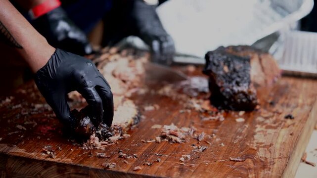 A juicy barbecued brisket being sliced on a wooden cutting board with a knife and tongs.
