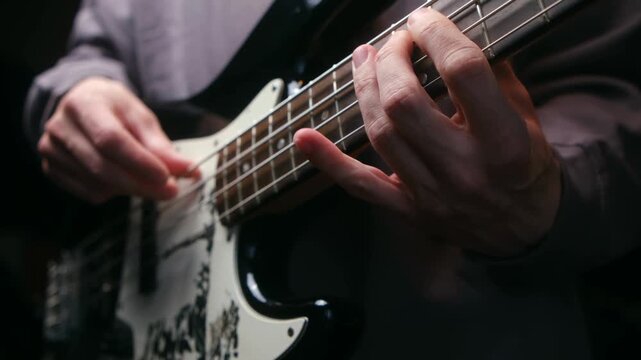 Talented musician playing an electric bass guitar during rehearsal or live concert. Close up bassist hands plucking fretting strings to create funky groove. Male musician playing electric bass guitar