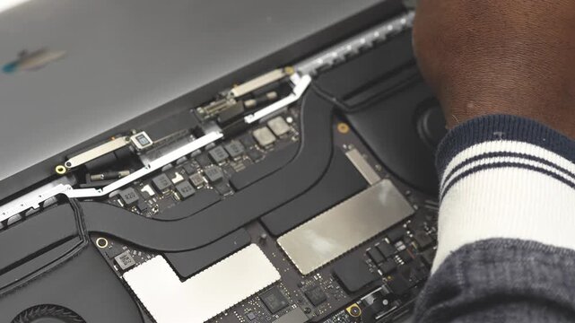 Technician repairing laptop motherboard with tools in electronics workshop environment