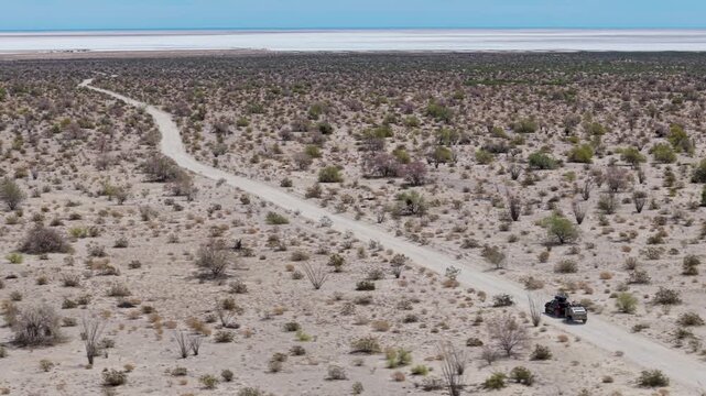 Aerial view shows an SUV towing a teardrop camper trailer across the dry Baja desert landscape near El Salar salt flats.