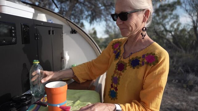 Mature woman prepares drinks in her teardrop camper trailer while camping in the desert of Baja California Mexico.