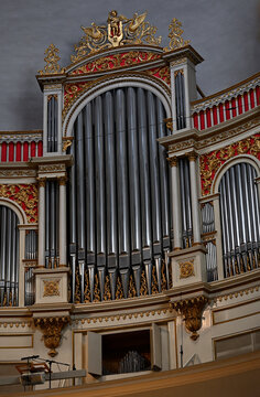 Ornate pipe organ with gilded decorations and red accents inside a historic church