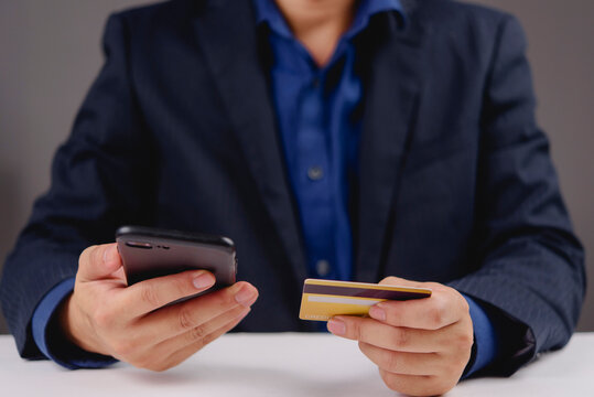 Businessman hands holding credit card and using smartphone for mobile payment. Male consumer shopping online with banking app technology. Secure digital transaction concept.
