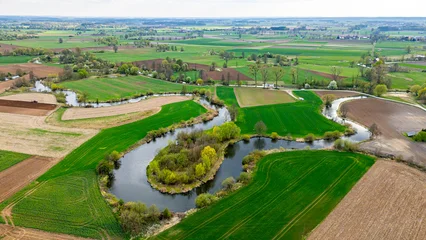 Fotobehang Groen Aerial drone shot of the Prosna river meanders winding through lush green agricultural fields and rural meadows, natural riverbed landscape, spring vegetation on the banks, bright daylight, top view.  © Adam