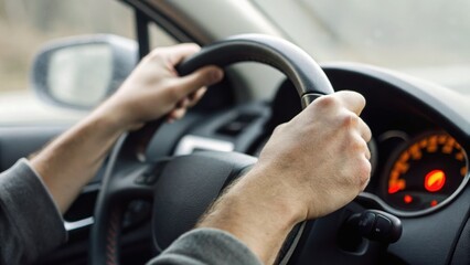 Naklejka premium Hands gripping a steering wheel inside a car, focusing on the driver's control and dashboard with illuminated gauges in the background.