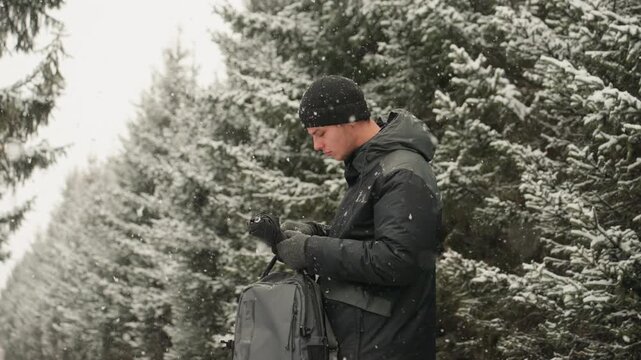 Caucasian man snowy trail adjusting backpack straps, focused expression with knitted hat and insulated coat, gloved hands, falling flakes, muted evergreen backdrop, purposeful pace and urban commute