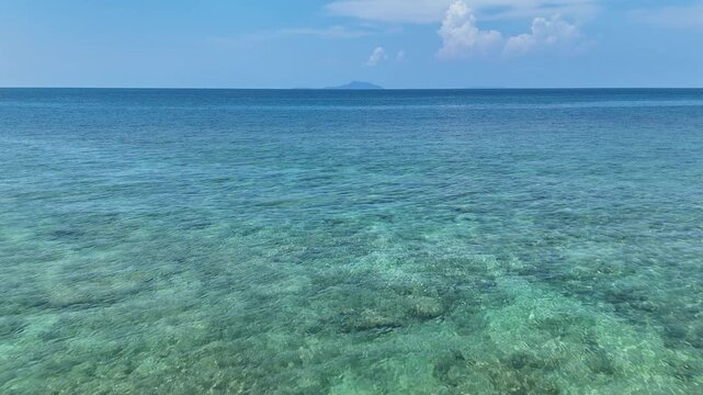 Serene View of Clear Turquoise Sea and Blue Sky with Distant Island on Horizon, Creating Tranquil Scene