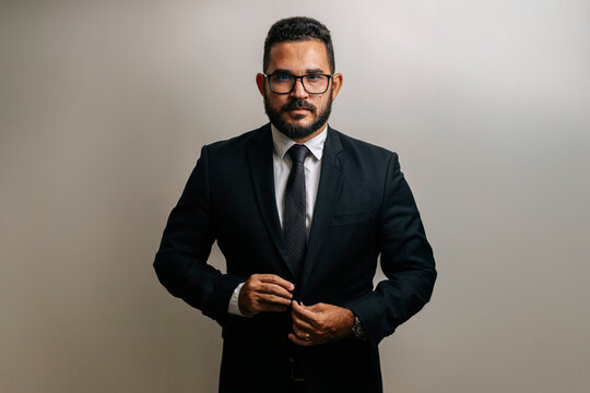 Confident businessman in formal suit adjusting jacket, posing against neutral background in a clean corporate portrait.