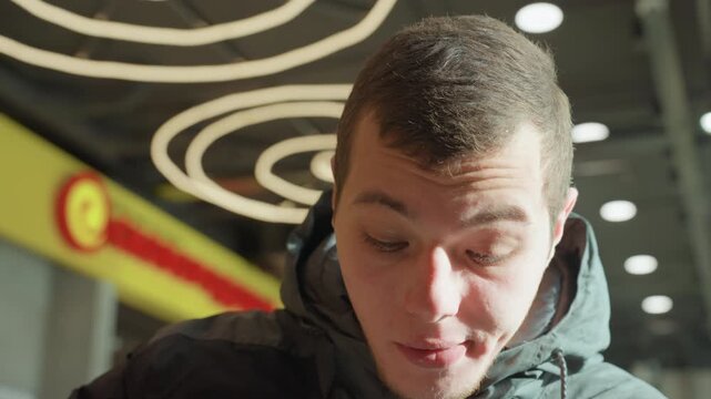 White male looking down in mall food court, wearing winter jacket beneath circular neon lights closeup portrait capturing tasting, focused and pensive expressions, student and traveler actions as he