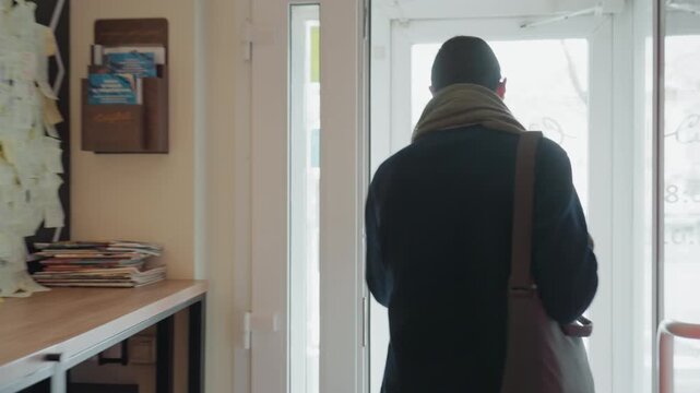 Man leaving cafe, back to camera, wearing scarf and shoulder bag commuter steps through doorway into bright street, quiet reflective mood, backlit silhouette and steady walk captured in sequence