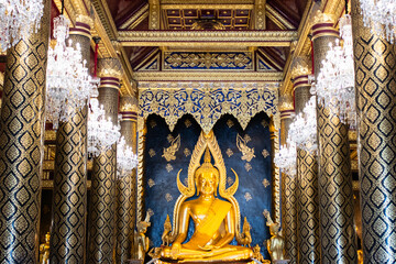 Obraz premium Golden Phra Phuttha Chinnarat Buddha statue in the ornate chapel of Wat Phra Si Rattana Mahathat with crystal chandeliers and golden pillars