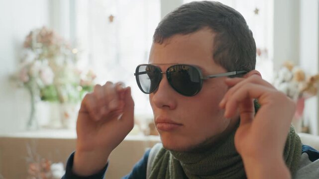 Caucasian male indoor adjusting sunglasses, sunlit window and floral decor frame a green scarf and calm profile sequential frames show fitting, settling, and confident posture with cinematic grain