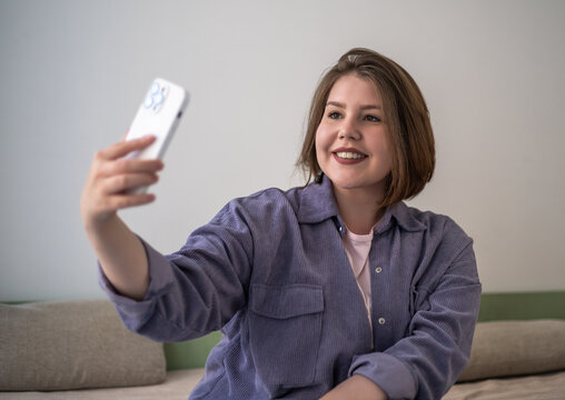 Selfie plus size woman smiling with smartphone, social media content creator, body positive confidence, video chat, influencer lifestyle at home.