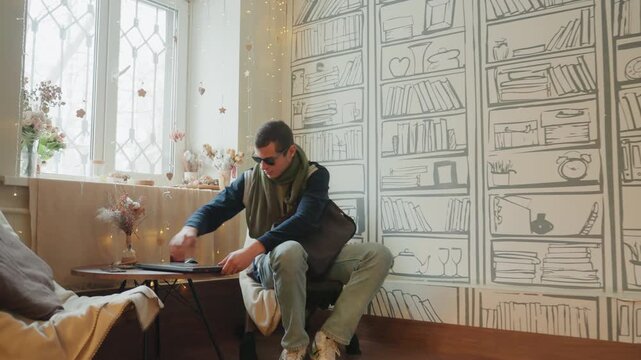 White man working laptop in livingroom. Sipping coffee, making quick phone call, adjusting bag on sofa, connecting charger to laptop, hands typing on keyboard, focused expression, modern boho