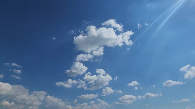 Sunbeams Piercing Through a Vibrant Blue Sky with Fluffy White Clouds